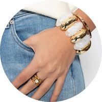 A hand wearing several gold and white bracelets, paired with a gold ring from SASSYCLASSY