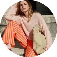 A woman is wearing wide-leg pants with an orange striped pattern, paired with a pink oversized sweater – fabric pants by SASSYCLASSY